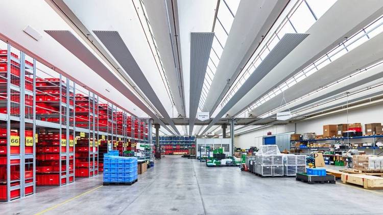 Alt-Text: „Innenansicht eines modernen Lagerhauses mit speziell angeordneten roten und blauen Regalsystemen zur effizienten Lagerung von Heizungs-, Lüftungs- und Klimatechnikprodukten, die unter strategisch platzierter LED-Leuchtenbeleuchtung präsentiert werden, um optimale Energieeffizienz zu demonstrieren.