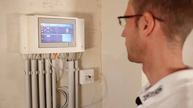 Alt-Text: „Techniker überprüft ein digitales Steuerungsmodul mit mehreren angeschlossenen Kabeln in einer modernen Heizungs- und Klimatechnikanlage.