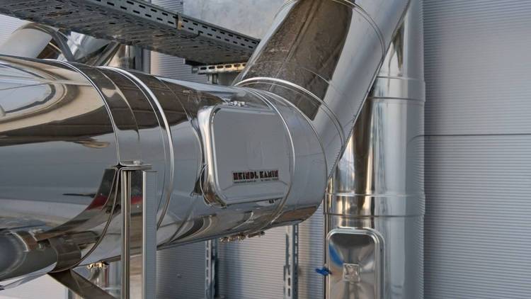 Alt-Text: „Nahaufnahme von glänzenden Metallrohren mit industriellen Armaturen in einer Fabrikumgebung, die moderne Lösungen für Heizung und Sanitärtechnik darstellen.