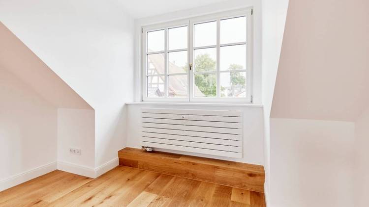 Alt-Text: „Ein heller leerer Raum mit Dachfenster, schräger Decke, weißen Wänden und Holzboden, ideal für die Implementierung energieeffizienter Heiz- und Kühlsysteme in der modernen Gebäudetechnik.“.