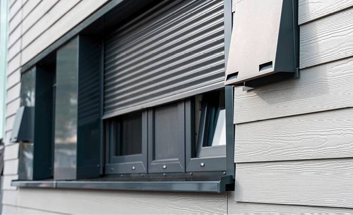 Alt-Text: „Nahaufnahme eines modernen Gebäudefensters mit halbgeschlossenen Sicherheitslamellen für verbesserte Energieeffizienz und Sonnenschutz.