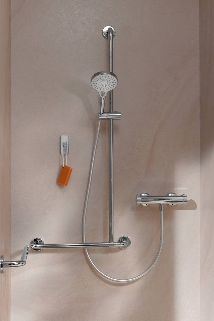 Alt-Text: „Moderne Dusche mit höhenverstellbarem Duschkopf, montiert an einer beigen Wand, ausgestattet mit einem horizontalen Haltegriff für barrierefreien Zugang und integrierter Seifenschale – ideal für Sanitärprojekte in der Gebäudetechnik.“.