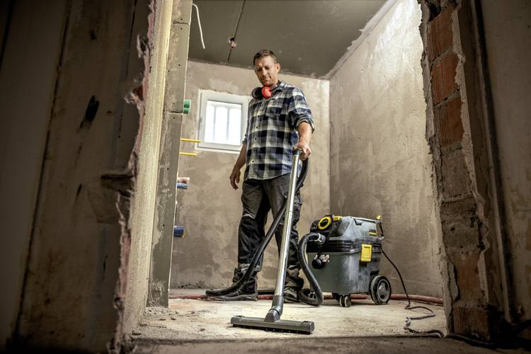 ALT-Text: „Fachkraft in der Gebäudetechnik saugt Baustelle mit Industriestaubsauger zur Vorbereitung von SHK-Installationen und zur Sicherstellung hoher Energieeffizienz durch saubere Arbeitsumgebung.