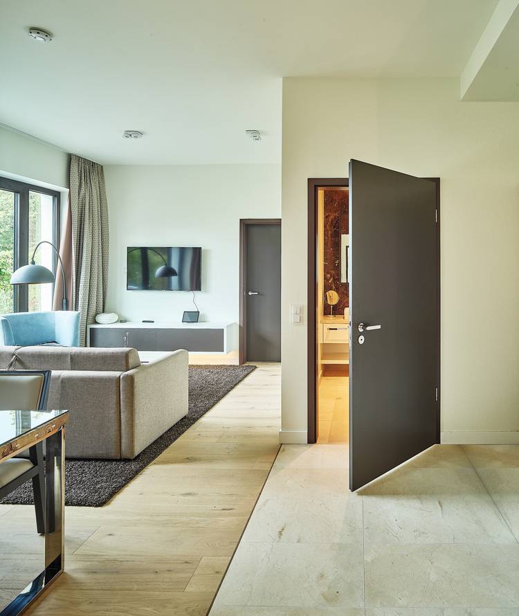 Bild einer modernen Wohnraumgestaltung mit grauem Sofa und wandmontiertem Fernseher, veranschaulicht energieeffiziente Bauweisen durch große Fenster für optimierte Lichtverhältnisse; relevant für Entscheider bei der Planung von energieeffizienten Gebäudetechnikkonzepten.