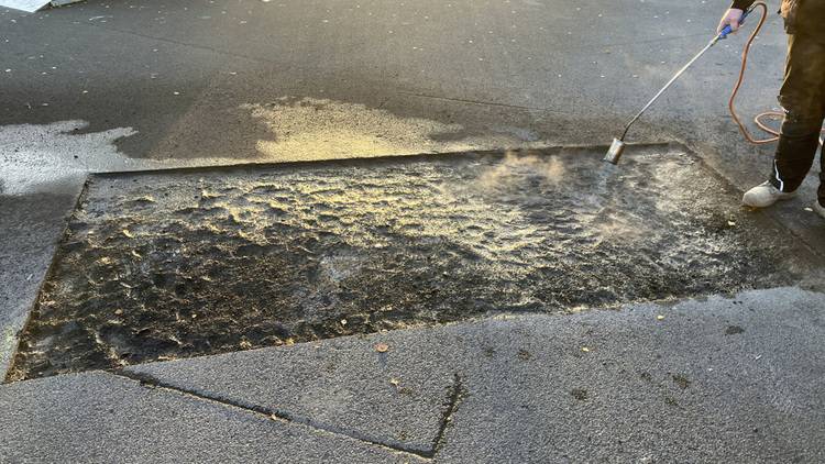 ALT-Text: Fachhandwerker erhitzt mit einem Gasbrenner eine Dachabdichtungsbahn zur nahtlosen Integration im Flachdachsystem eines energieeffizienten Gebäudes.