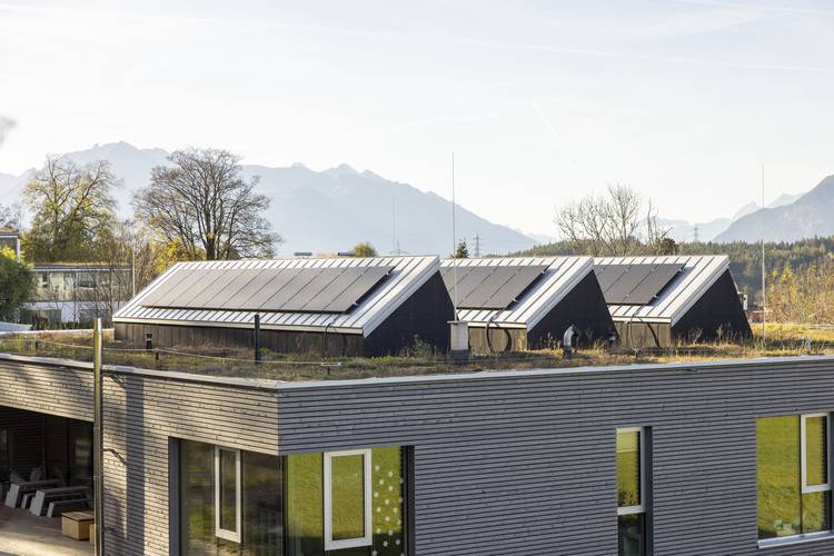 Moderne Gebäude mit Solarzellen auf dem Dach betonen die Nachhaltigkeit in der Gebäudetechnik, umgeben von einer malerischen Berglandschaft unter klarem Himmel.