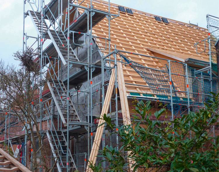 Alt-Text: „Gebäudetechnik-Baustelle mit umfassendem Gerüst zur Installation moderner Dachkonstruktion, zeigt Fortschritt in der Energieeffizienzsteigerung bei bewölktem Himmel.