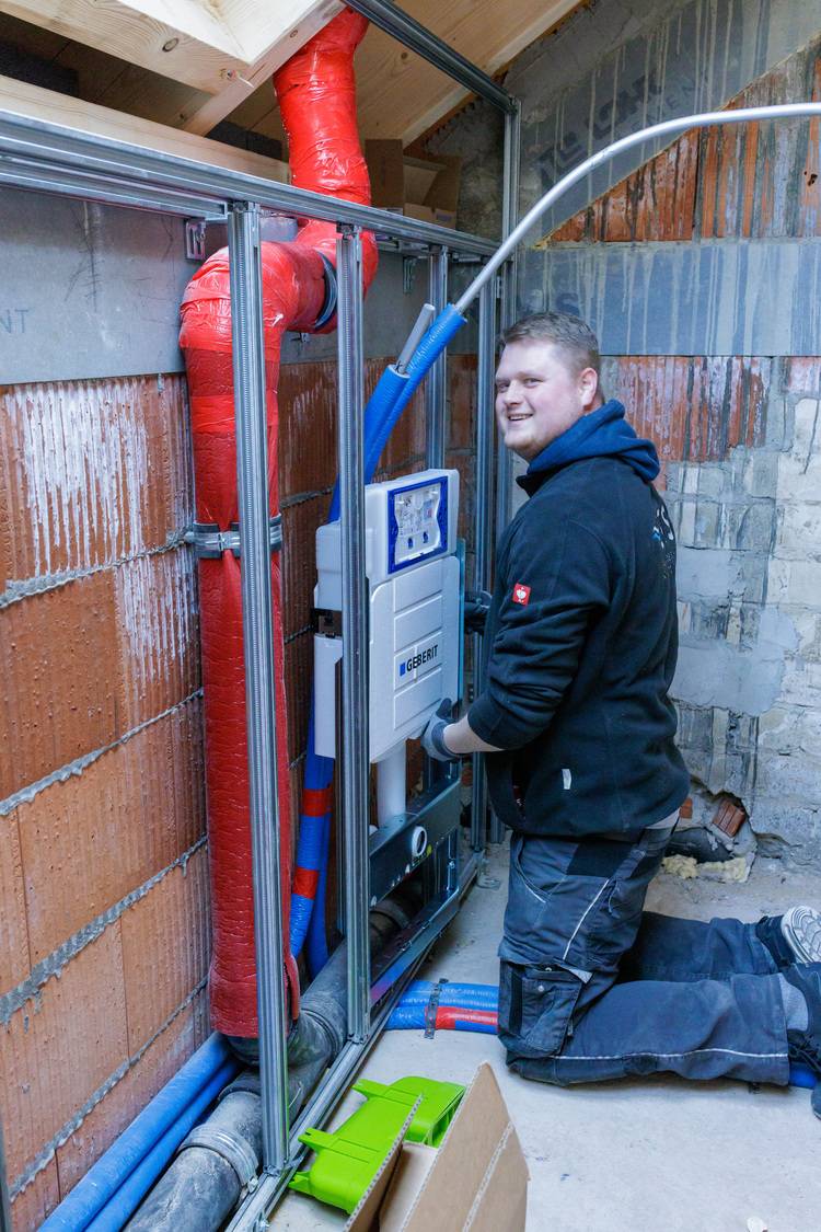 Alt-Text: „Fachhandwerker installiert moderne Sanitärtechnik in einem Rohbau, umgeben von Rohrleitungen und Isolationsmaterialien für energieeffizientes Gebäudemanagement.“.