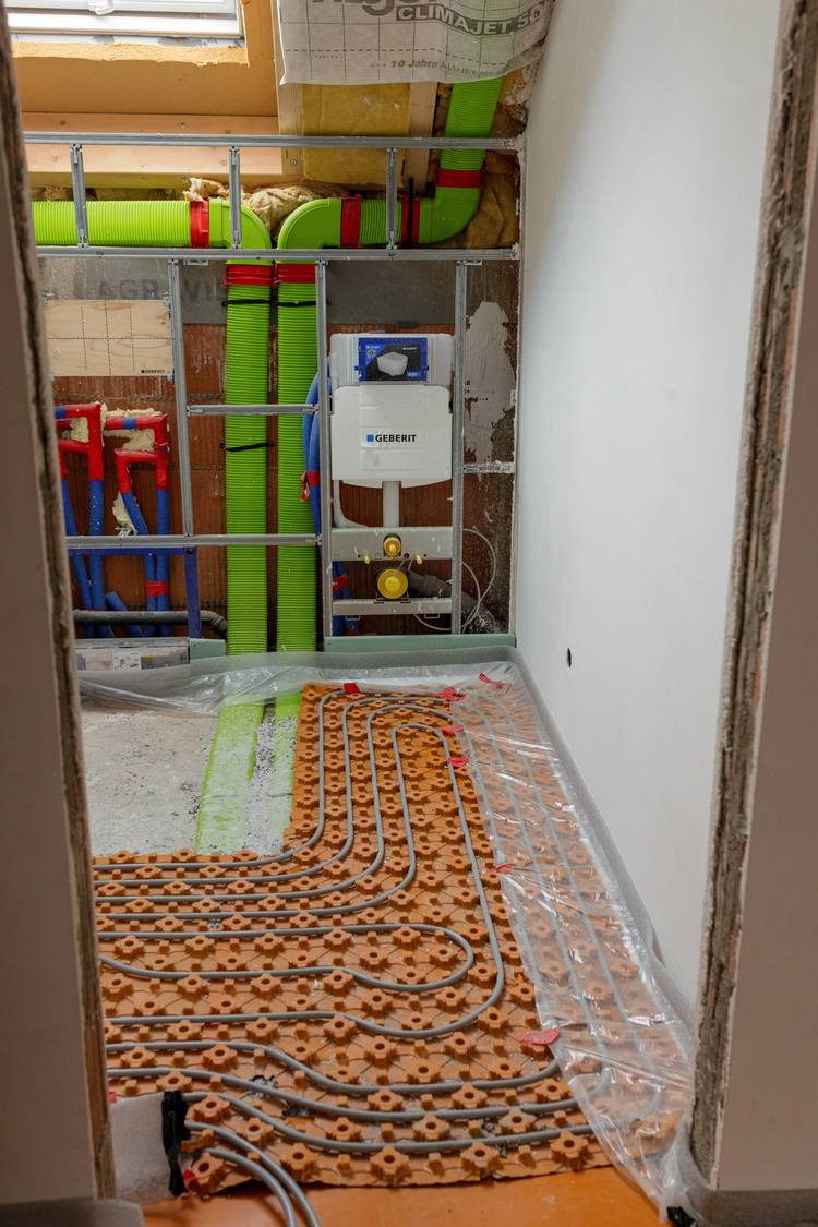 Baustelle eines Badezimmers mit freiliegenden Sanitärinstallationen und fortschrittlichem Fußbodenheizungssystem, geeignet für energieeffiziente Gebäudeplanung im SHK-Bereich.