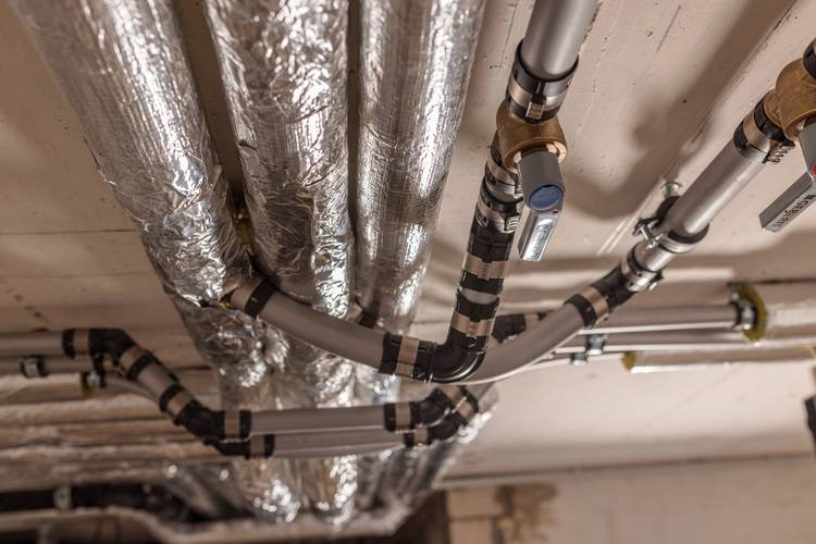 Verschiedene gedämmte Rohrleitungen und Ventile an einer Decke installiert zur Optimierung der Energieeffizienz in modernen Gebäudetechniksystemen.