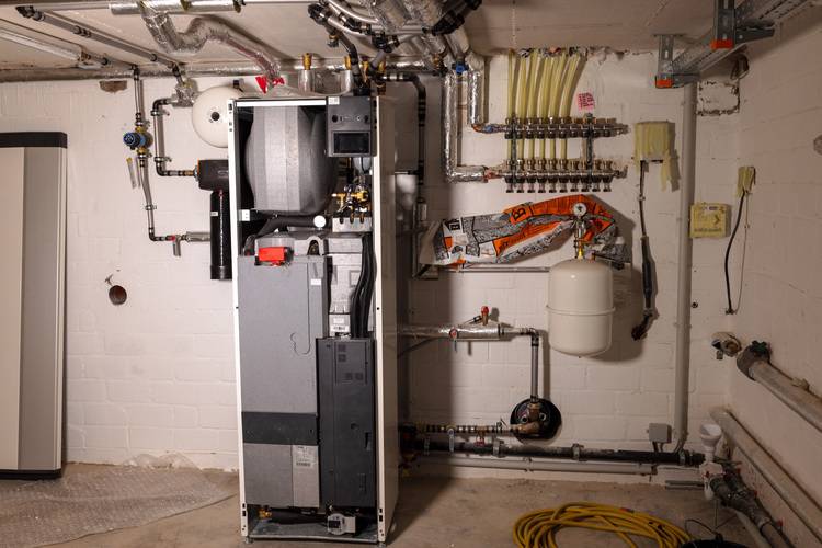 ALT-Text: „Heizungsanlage im Keller mit modernen Rohrleitungen, Regelventilen und einem Ausdehnungsgefäß an einer weißen Backsteinwand, symbolisiert effiziente Systemintegration für Entscheider in der Gebäudetechnik.