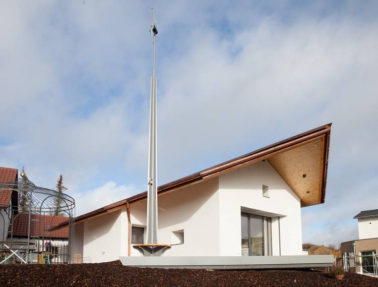 „Energieeffizientes Gebäude mit Holzdach, großem Fenster und hoher Windturbine, ideal für nachhaltige Gebäudetechniklösungen.