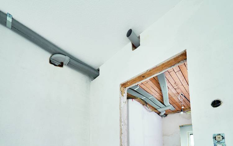 Ein unvollendeter Raum mit offenen Deckenbalken und sichtbaren Lüftungskanälen vor weißen Wänden, der den Fortschritt moderner TGA-Installationen in einem Gewerbegebäude zeigt.