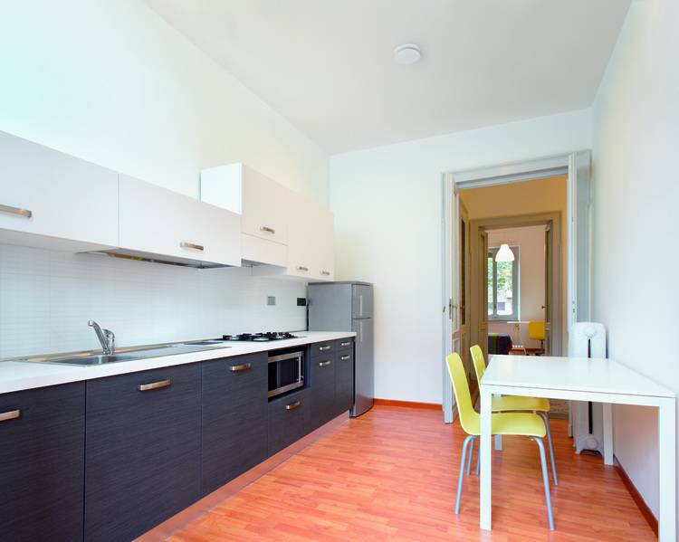 Moderne Küche mit energieeffizienter Lüftungsanlage, weißen und dunklen Schränken. Essbereich mit grünen Stühlen auf Holzboden. Türöffnung führt zu angrenzendem Raum, ideal für Fachhandwerker und Gebäudeplaner zur Integration nachhaltiger Technikkonzepte.