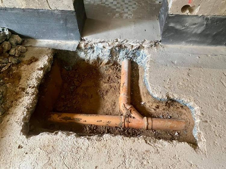 „Offene, isolierte Rohrleitungen für ein energieeffizientes Heizsystem in einem freigelegten Bereich einer Betonbodenplatte auf einer Baustelle, die moderne Gebäudetechnik hervorhebt.“.