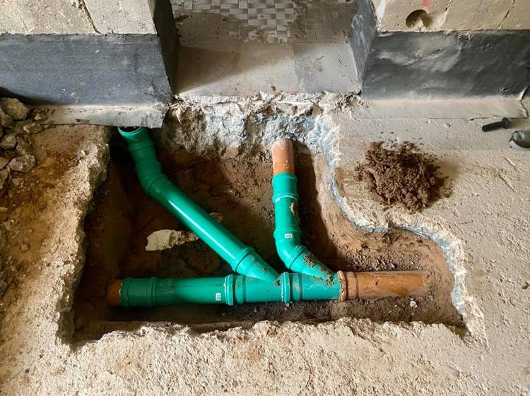 „Offenliegende Sanitärrohre in einem Bodenschacht, umgeben von Beton und einem Erdhaufen rechts – Beispiel für die Installation in der Gebäudetechnikbranche.