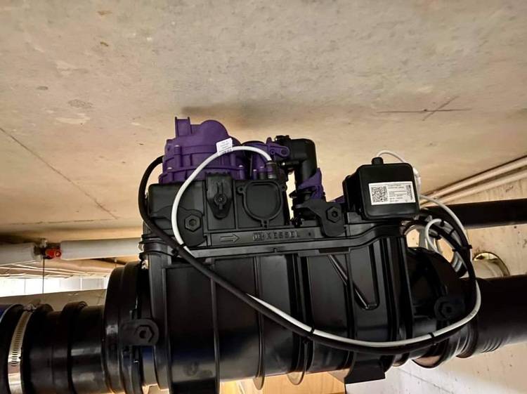 „Digitale Steuerungseinheit für Heizungsanlage mit lila Komponenten und Kabelverbindungen, montiert an einem Leitungsrohr in der Nähe der Decke, zur Optimierung der Energieeffizienz in Gebäudetechniksystemen.