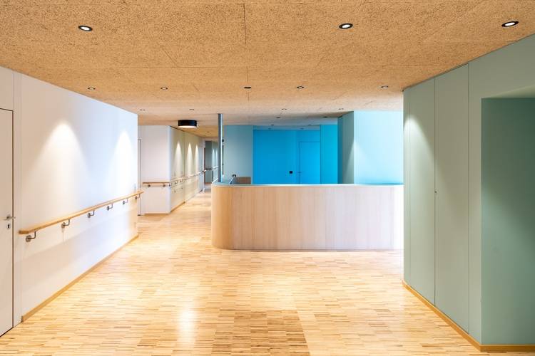 „Moderne Eingangshalle in einem energieeffizienten Gebäudekomplex mit umweltfreundlichem Holzfußboden, nachhaltigem Empfangstresen aus hellem Holz und Wänden in energetisierendem Blaugrün, beleuchtet durch innovative LED-Deckenbeleuchtung.