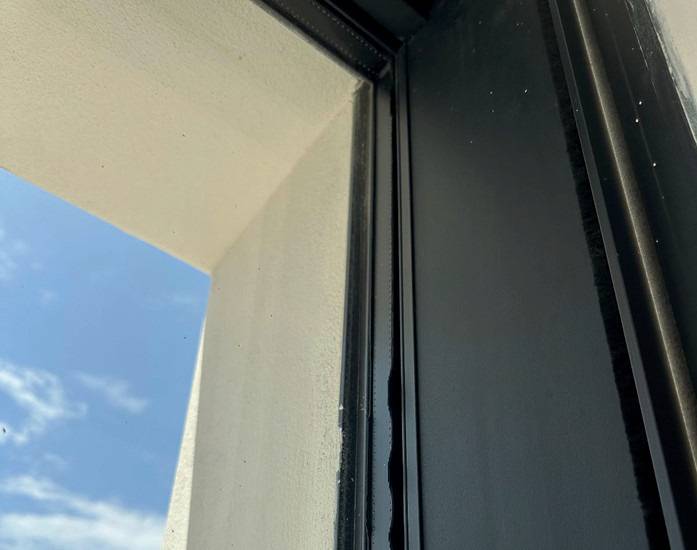 Sicher! Hier ist ein optimierter ALT-Text, ausgerichtet auf die Zielgruppe und die Themen von haustec.de: „Detailansicht eines modernen schwarzen Fensterrahmens mit energieeffizienter Verglasung, durch den Tageslicht sowie blauer Himmel mit Wolken in einem energieoptimierten Gebäude sichtbar sind.“ Dieser ALT-Text beschreibt nicht nur das Bild, sondern betont relevante Aspekte wie Energieeffizienz und moderne Gebäudetechnik.