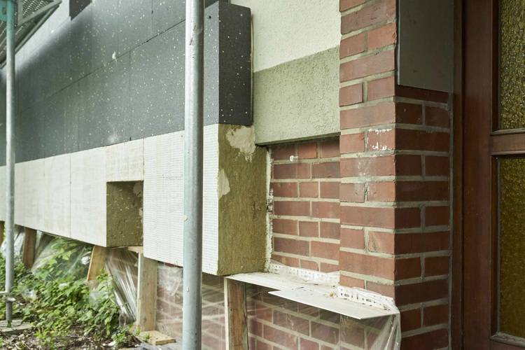 „Nahaufnahme einer unfertigen Gebäudefassade mit sichtbaren Dämmstoffschichten und Mauerwerk, zeigt fortgeschrittene Technologien für Energieeffizienz in der Gebäudehülle.