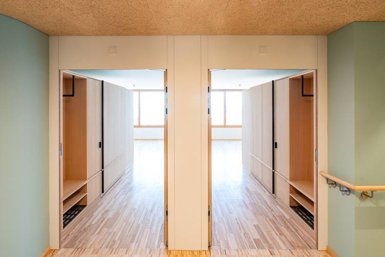 „Moderne Büroetage in einem energieeffizienten Gebäude mit hellen Holzfußböden und Glasabtrennungen, die zu einem lichtdurchfluteten Besprechungsraum führen. Ideal für Architekten und Facility Manager, die nachhaltige Lösungen und barrierefreie Designs in der Gebäudetechnik umsetzen.