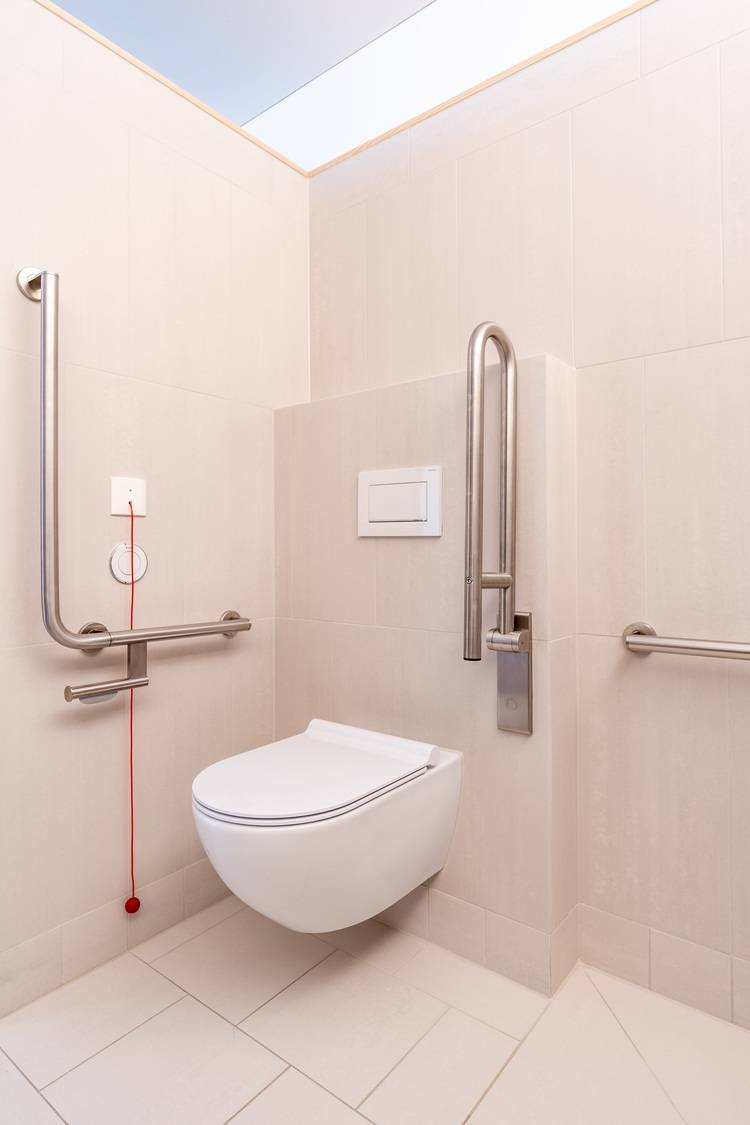 Barrierefreies WC mit wandhängendem WC, stabilen Haltegriffen und Notrufleine in einer modernen Sanitärinstallation für barrierefreie Gebäudeinfrastruktur.