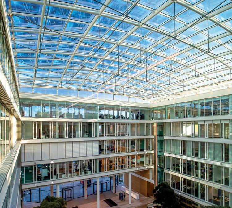 Barriereoptimierter, themenrelevanter ALT-Text für haustec.de (Gebäudetechnik): „Innenansicht eines modernen Bürogebäudes mit verglastem Atrium, mehreren offenen Etagen und hell belichteten Laufwegen; sichtbare energieeffiziente Gebäudetechnik wie Lüftungs- und Heizsysteme im Deckenbereich.“.