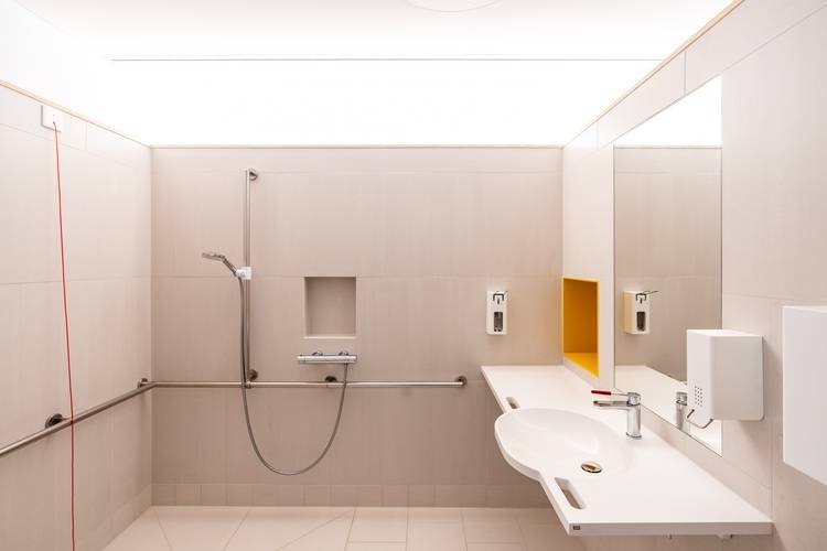 „Barrierefreies Badezimmer mit bodengleicher Dusche, wandmontiertem Waschbecken, Haltegriffen und berührungslosen Seifenspendern, ideal für den Einsatz in modernen Technikprojekten im Hinblick auf Barrierefreiheit und Komfort.