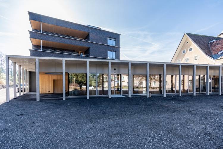 „Modernes Bürogebäude mit großflächigen Glasfassaden und überdachtem Zugangsgang, neben einem mehrstöckigen Bauwerk. Symbolisiert innovative Gebäudetechniklösungen für Energieeffizienz und nachhaltige Architektur in der TGA-Branche.