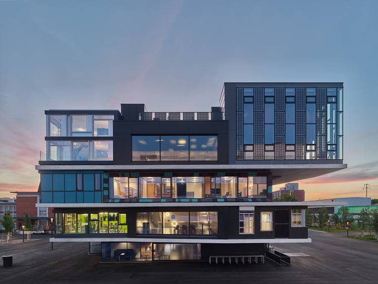 Barrierefreier ALT-Text: „Modernes mehrgeschossiges Bürogebäude mit großen Glasfassaden und auskragenden Elementen, Beispiel für energieeffiziente Gebäudehülle in der gewerblichen Gebäudetechnik.“.