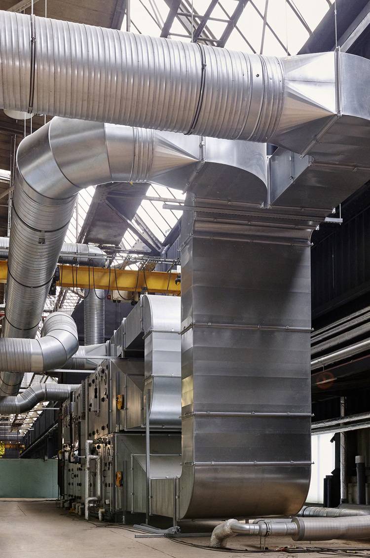 „Industrie-Lüftungssystem mit großen Metallkanälen in einer Fabrikumgebung, ideal für effiziente Klimatisierung und Luftqualität in gewerblichen Gebäuden.