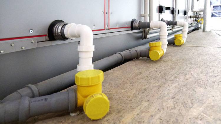 „Rohrleitungen mit gelben Schutzkappen, die an ein leistungsstarkes Deckenlüftungssystem in einem industriellen Innenbereich angeschlossen sind, optimiert für effiziente Energieverteilung und Klimasteuerung in gewerblichen Gebäuden.