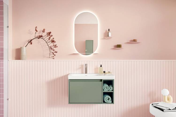 Moderner Sanitärraum mit pastellrosa Wänden, ovalem Spiegel und grünem Waschbeckenunterschrank, gestaltet für energieeffiziente Gebäudekonzepte in der Haustechnik.