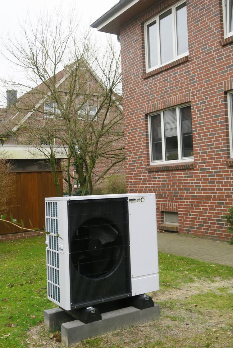 Außeneinheit einer Wärmepumpe für die Heizungs- und Klimatechnik, installiert neben einem Wohngebäude aus Klinkerstein; Sichtbar ist auch eine für Energieeffizienz relevante Freifläche in einem modernen Gebäudetechnik-Kontext.