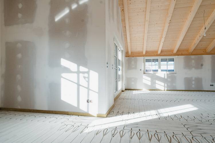 Alt-Text-Vorschlag: "Heller, unfertiger Technikraum mit freiliegender Holzdecke, weißen Wänden und großflächigen Fenstern, durch die Tageslicht auf die künftige Installationsebene für Gebäudetechnik wie Lüftung, Heizung oder Elektroanlagen fällt.