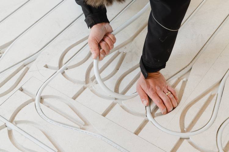 Optimierter ALT-Text: "Fachkraft verlegt flexible Kunststoffrohre in vorbereitete Rillen einer gedämmten Bodenplatte zur Installation einer energieeffizienten Fußbodenheizung im Neubau, typischer Arbeitsschritt in der modernen Gebäudetechnik.