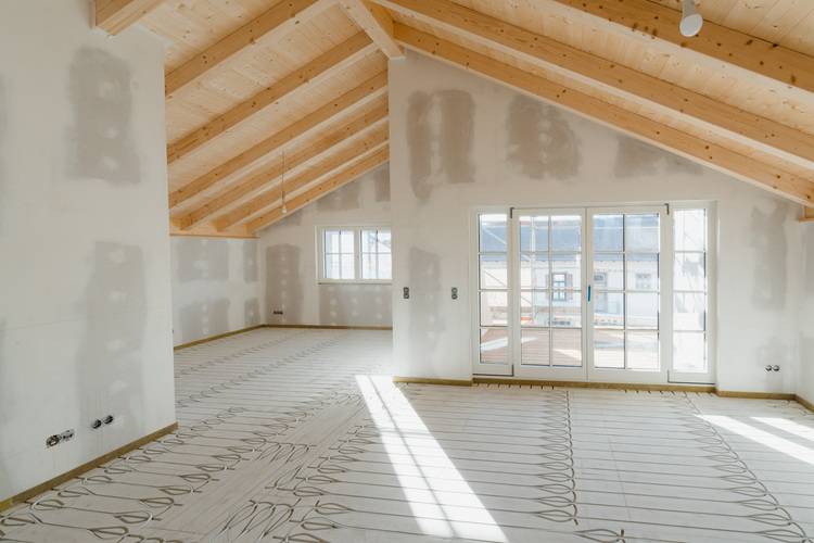 Alt-Text-Vorschlag: "Unfertiger Dachausbau mit sichtbaren Holzbalken, großflächigen Fenstern und installiertem System zur Fußbodenheizung - Beispiel moderner energieeffizienter Gebäudetechnik für TGA-Planung im Wohnungsbau.