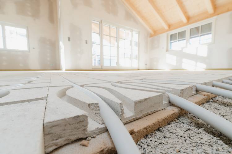 Optimierter ALT-Text: "Detailaufnahme der Installation von Fußbodenheizungsrohren auf Dämmplatten in einem hellen, rohbauartigen Raum mit großen Fenstern - typische Arbeitsschritte für SHK-Fachbetriebe bei energieeffizienten Neubauten oder Sanierungen.