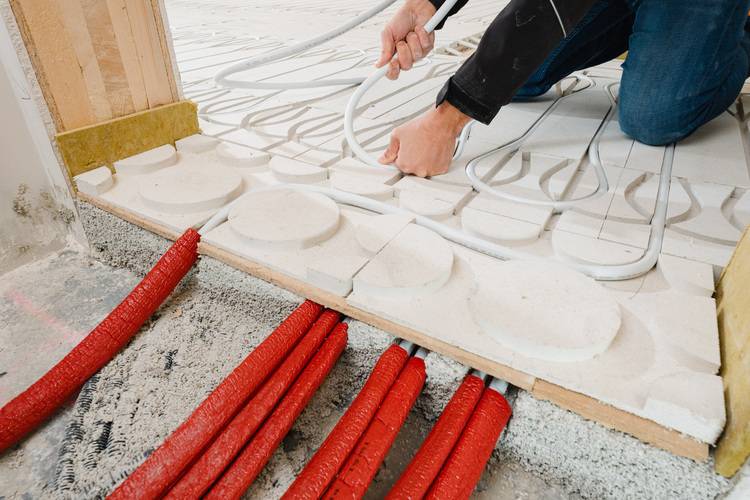 Optimierter ALT-Text: "Fachhandwerker verlegt flexible weiße Fußbodenheizungsrohre auf Dämmplatten bei der Installation moderner Flächenheizung in einem Neubau - Vorbereitung energieeffizienter Wärmeverteilung im Gebäudetechnik-Projekt.