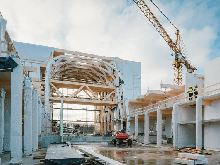 Barrierefreier, optimierter ALT-Text für haustec.de: „Rohbau eines modernen Gebäudes mit sichtbaren Holzträgern; auf der Baustelle sind Facharbeiter in Sicherheitskleidung beim Einbau energieeffizienter Haustechnik zu sehen, während ein Kran Baumaterialien bewegt.“.