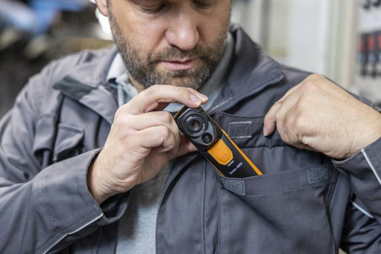 Gerne! Hier ist ein optimierter, barrierefreier und zielgruppenspezifischer ALT-Text für das beschriebene Bild: "Fachhandwerker steckt eine kompakte Wärmebildkamera zur Heizungsinspektion in die Brusttasche seiner Arbeitsjacke." Optional, je nach Kontext des Artikels, kann der Text weiter spezifiziert werden, z.B.: "SHK-Fachmann verstaut modernes Messgerät zur Leckageortung in Gebäudetechnik-Anlagen in die Brusttasche seiner Arbeitskleidung." Dadurch wird sowohl das Gerät als auch der Anwendungsbezug zur Gebäudetechnik und die Zielgruppe deutlich.