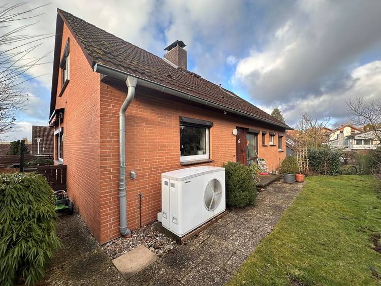 Sicher, hier ist ein optimierter, themenspezifischer ALT-Text für das beschriebene Bild auf haustec.de: Alt-Text: Einfamilienhaus aus Klinker mit außen aufgestellter Luft-Wärmepumpe neben Terrasse und Rasen; Beispiel für energieeffiziente Gebäudetechnik im Wohnbau. Begründung der Optimierung: - Der Text benennt die Gebäudetechnik-Komponente (Luft-Wärmepumpe). - Er nimmt Bezug auf den Anwendungsbereich (energieeffizienter Wohnbau/Gebäudetechnik). - Die Begriffe sind fachlich korrekt und suchmaschinenoptimiert für die Zielgruppe. - Überflüssige Bildelemente wie "wolkenverhangener Himmel" werden weggelassen. - Fokus liegt auf Relevanz für Entscheider und Fachkräfte in der Gebäudetechnik.