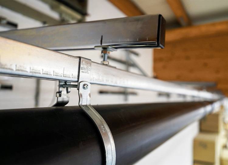 Detailansicht: Metallmontageschellen befestigen ein schwarzes Installationsrohr an einer Deckenunterkonstruktion in einem Gebäudetechnikprojekt.
