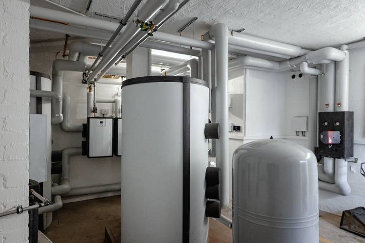 Heizungsraum mit großvolumigen Pufferspeichern, Rohrleitungen und Heiztechnikkomponenten für die zentrale Wärmeversorgung in einem Gebäude.