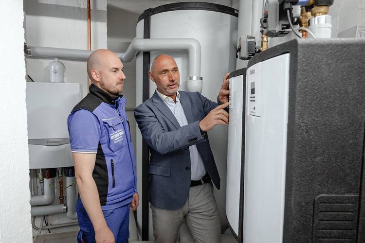 Zwei Fachkräfte prüfen und besprechen eine moderne Heizungsanlage in einem Technikraum, Fokus auf effiziente Gebäudetechnik und Beratung.