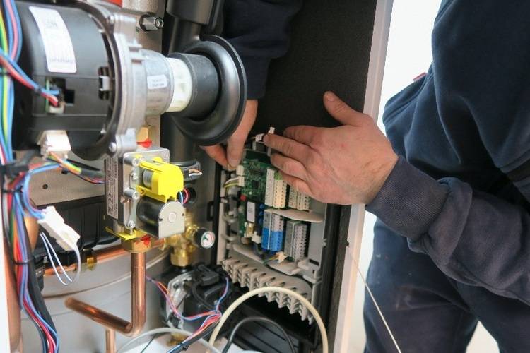 Fachperson prüft die Elektronik im Inneren eines Heizungs- oder Lüftungsgeräts, typisch bei Wartung in der Gebäudetechnikbranche.