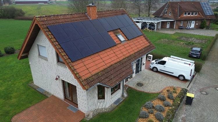 Wohngebäude mit Photovoltaikanlage auf dem Dach, zwei Servicefahrzeuge im Zufahrtsbereich, Beispiel für moderne Energie- und Gebäudetechnik.