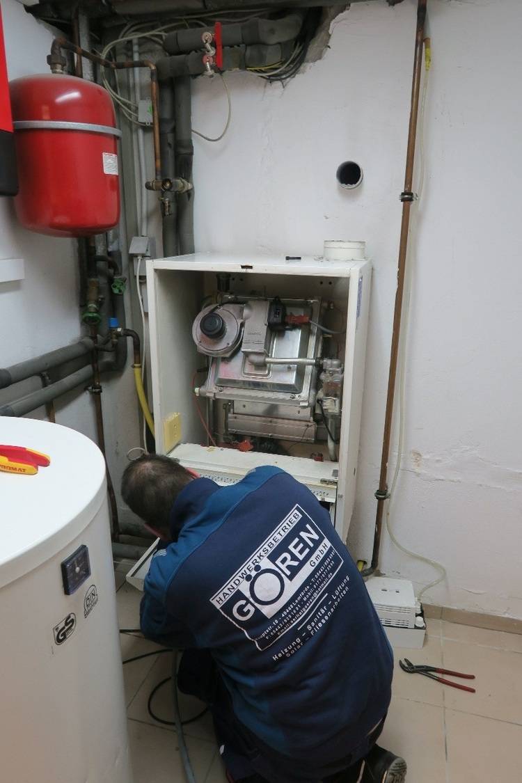 SHK-Fachkraft bei der Wartung eines gasbetriebenen Heizkessels im Technikraum, umgeben von Rohrleitungen, Armaturen und Installationswerkzeug.