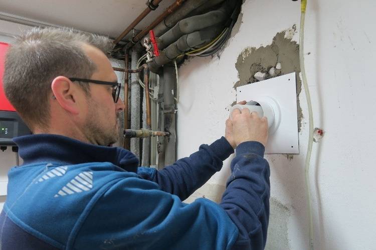 Fachhandwerker montiert ein Lüftungsrohr mit weißer Montagescheibe in eine Gebäudewand - Anwendung im Bereich Wohnraumlüftung.