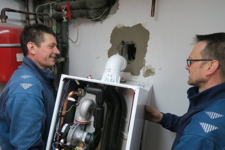 Fachhandwerker montieren ein Heizgerät an einer Wand mit sichtbaren Rohrleitungen in einem Technikraum - Fokus auf Installationstechnik Gebäudetechnik.